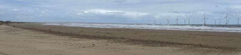 A sandy beach with waves in the background with Camber Sands in the background

Description automatically generated