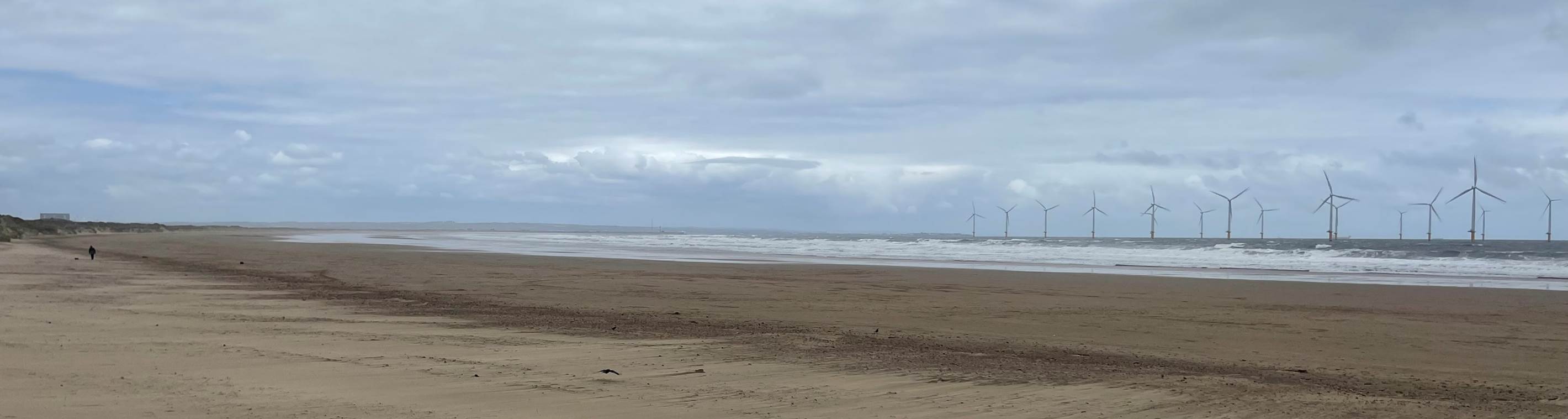 A sandy beach with waves in the background with Camber Sands in the background

Description automatically generated