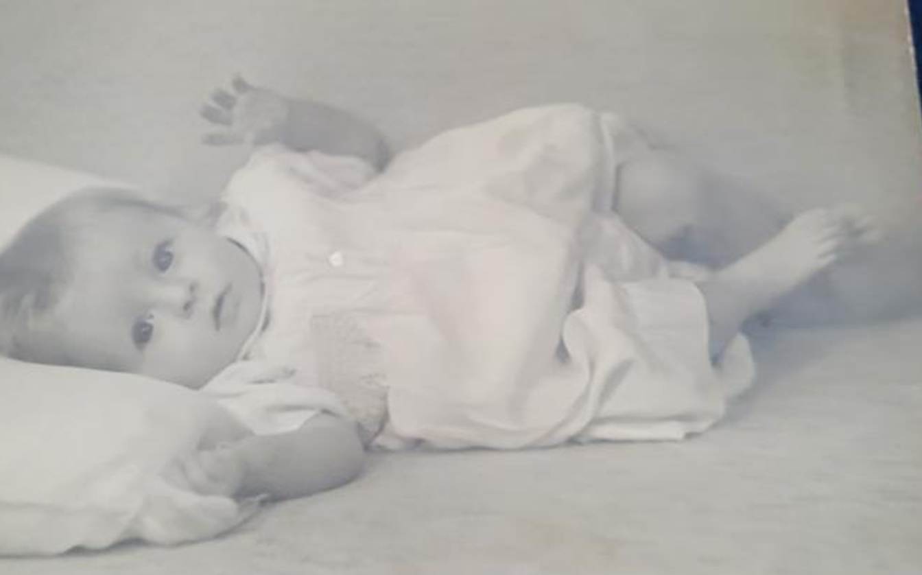 A black and white photo of a baby lying on a blue blanket

Description automatically generated