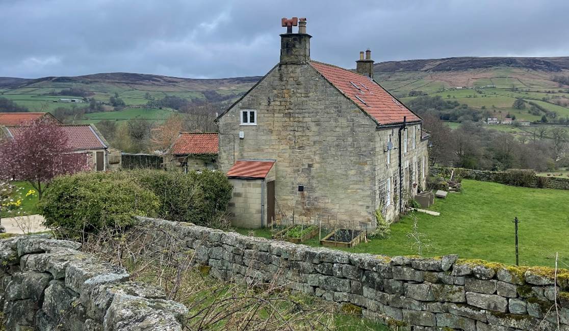 A stone house with a stone wall and grass

Description automatically generated