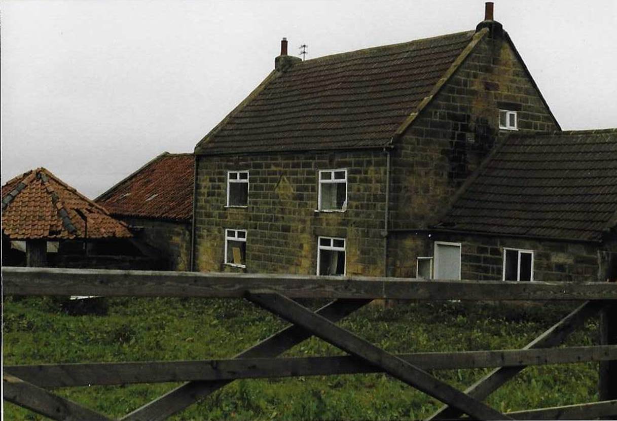 An old brick building with grass in front of a house

Description automatically generated