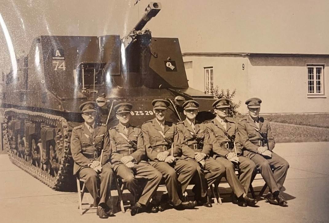 A group of men in uniform sitting in front of a tank

Description automatically generated