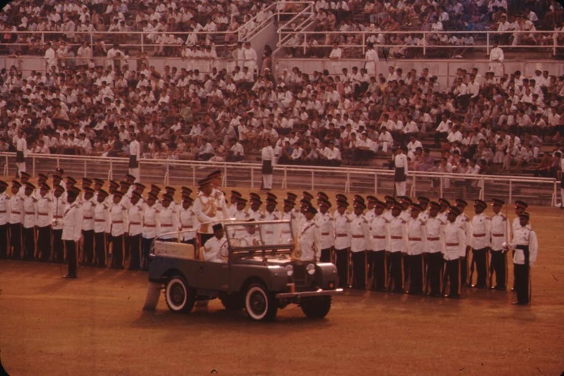 A military parade in front of a crowd

Description automatically generated