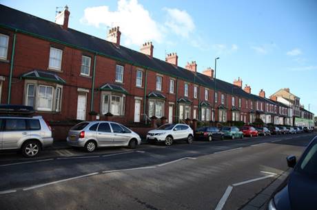 Long row of houses with cars parked on the side of the road

Description automatically generated