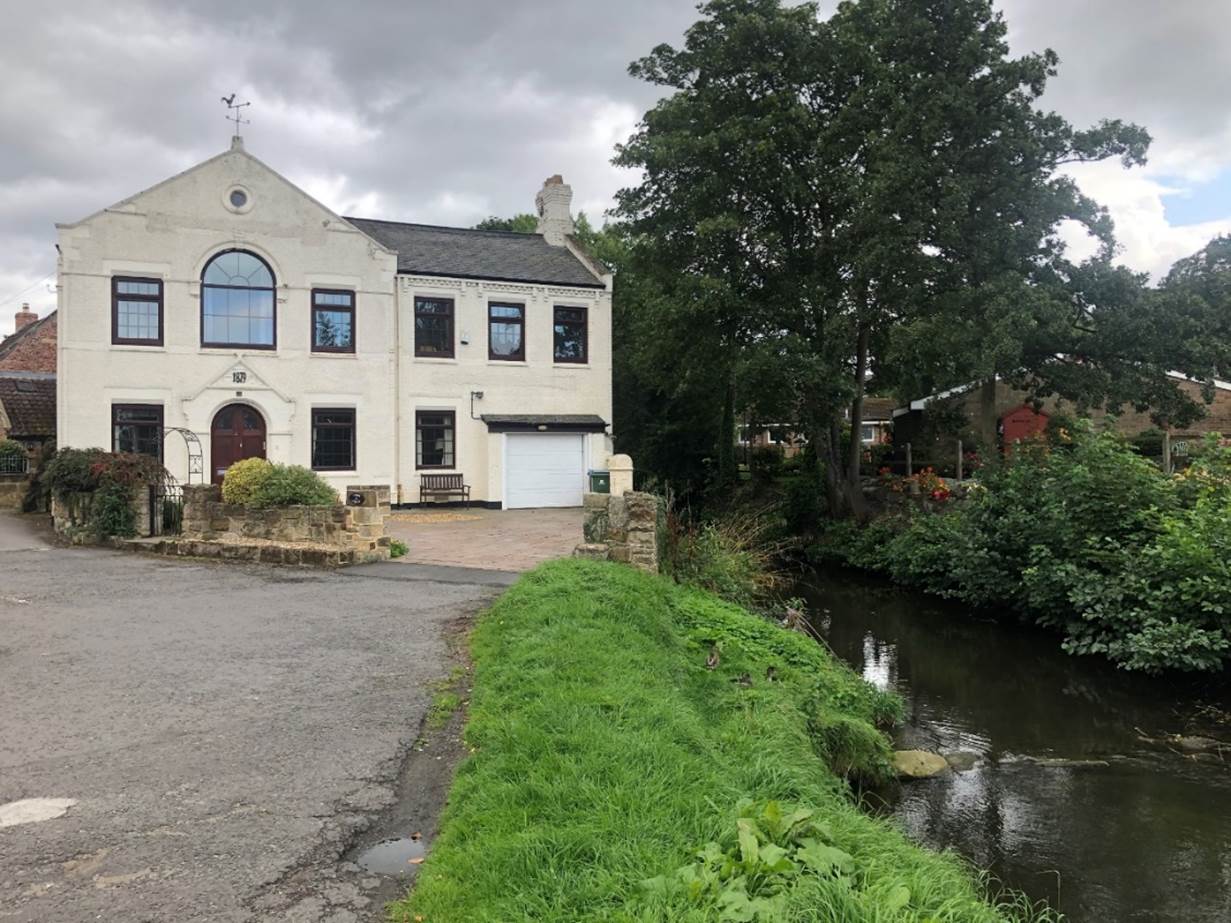 A white building with a river in the background

Description automatically generated