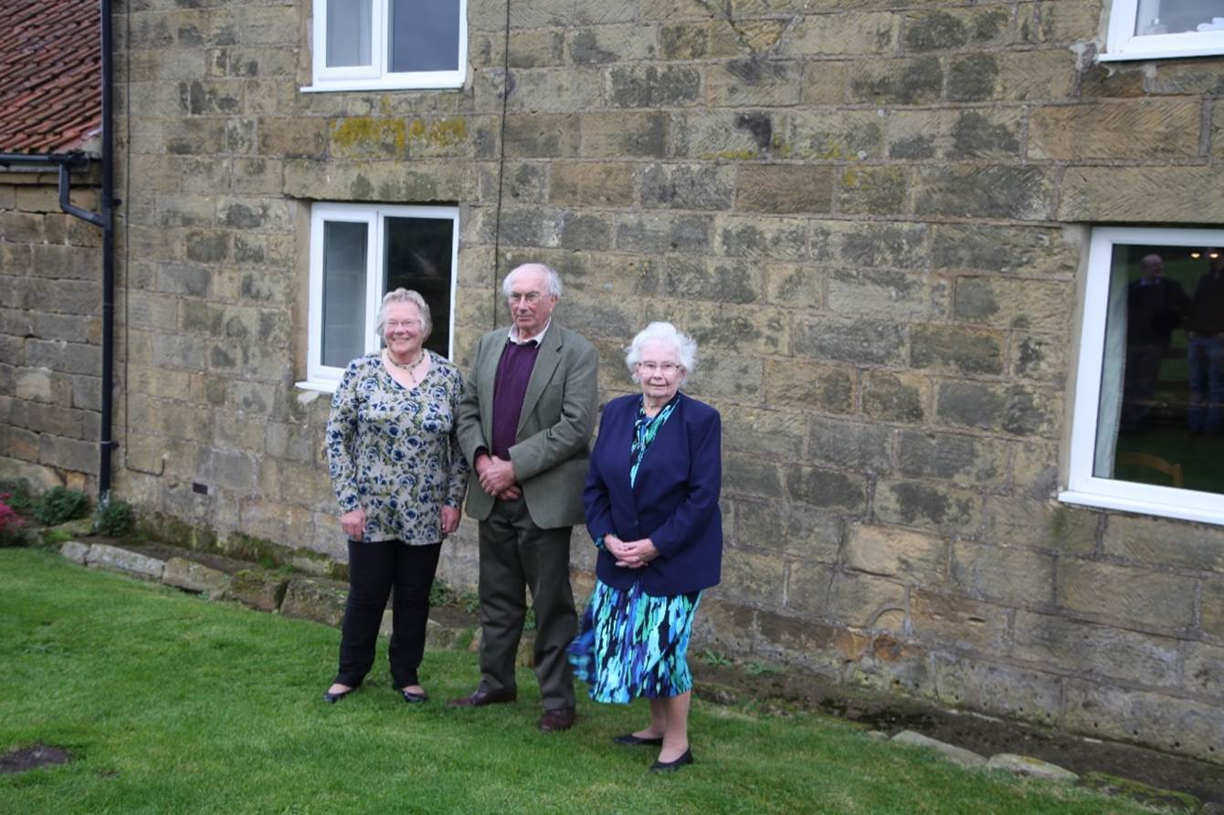 A group of old people standing in front of a stone building

Description automatically generated