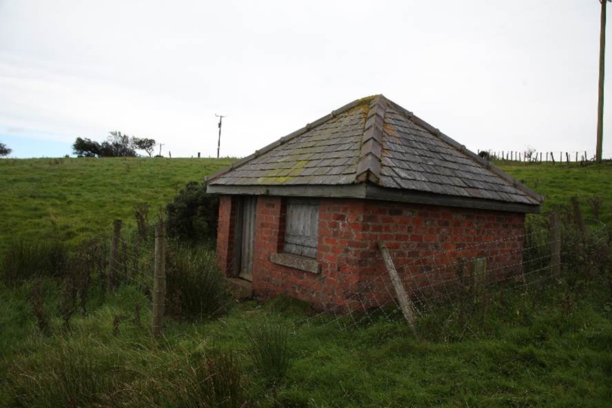 A small brick building in a grassy field

Description automatically generated