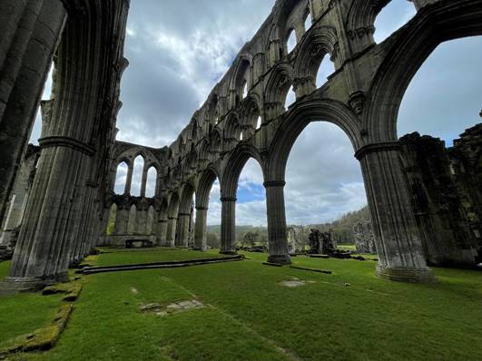 An old building with arches and grass

Description automatically generated