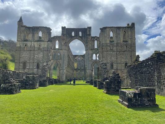 A stone building with arches and a green lawn

Description automatically generated