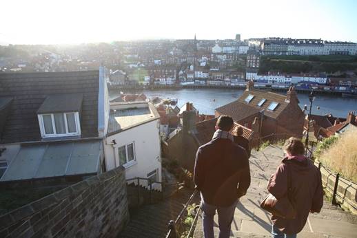 People walking down a hill with buildings and a river

Description automatically generated