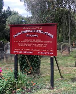 A sign over a grassy area with trees in the background

Description automatically generated